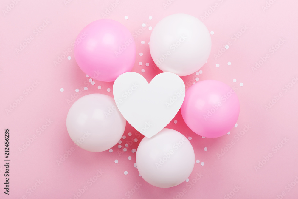 Birthday or wedding mockup with white heart shape, confetti and pastel balloons on pink table top view. Flat lay composition.