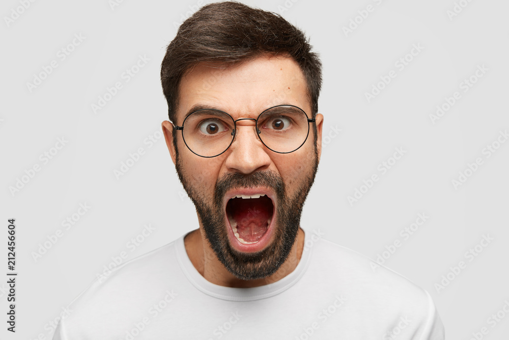 Aggressive attractive male shouts furiously, being annoyed with bad service, argues with director of company, can`t stop negative feeling, isolated over white background. People and anger concept