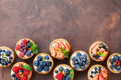 Delicious berry tartlets or cake with cream cheese decorated lemon peel and mint leaf from above Fototapet