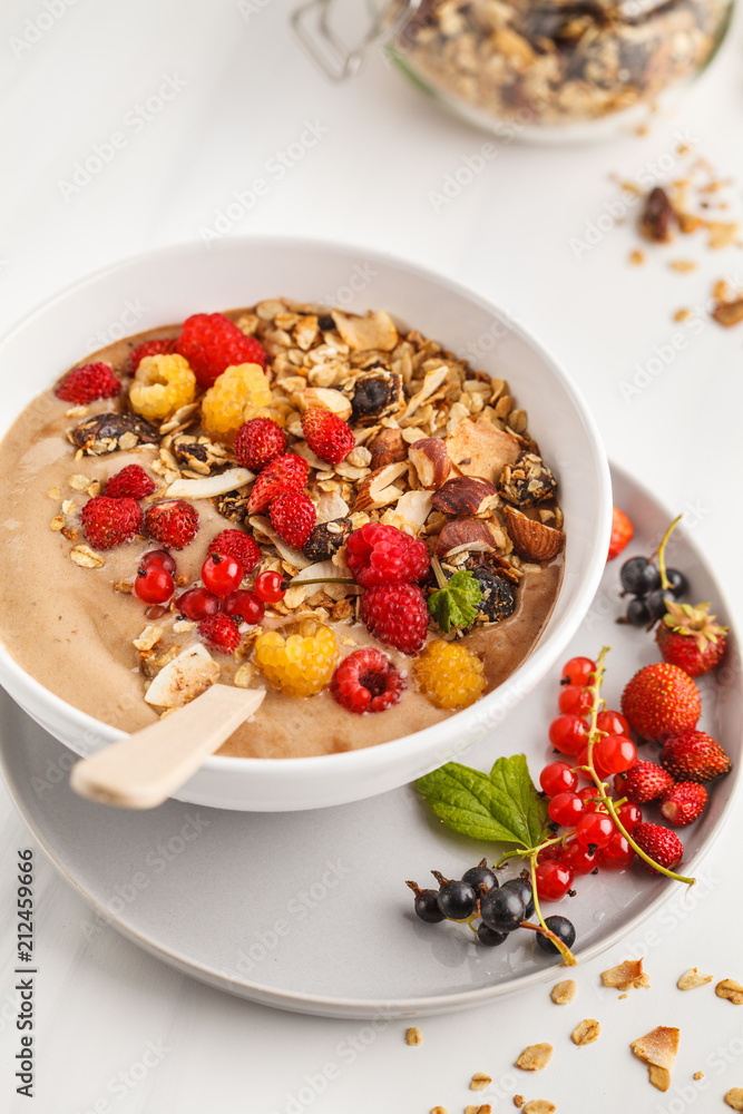 Smoothie bowl with banana, cocoa, berries and homemade granola, white background, vertical. Healthy vegan food concept. Smoothie bowl with banana, cocoa, berries and homemade granola, white background, vertical. Healthy vegan food concept.