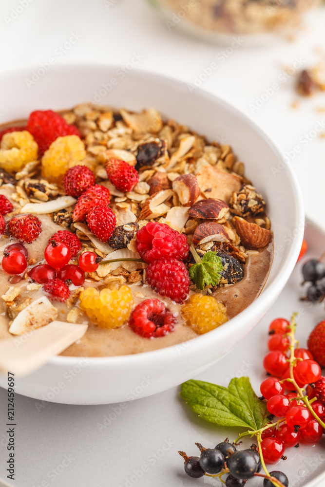 Smoothie bowl with banana, cocoa, berries and homemade granola, white background, vertical. Healthy vegan food concept. Smoothie bowl with banana, cocoa, berries and homemade granola, white background, vertical. Healthy vegan food concept.