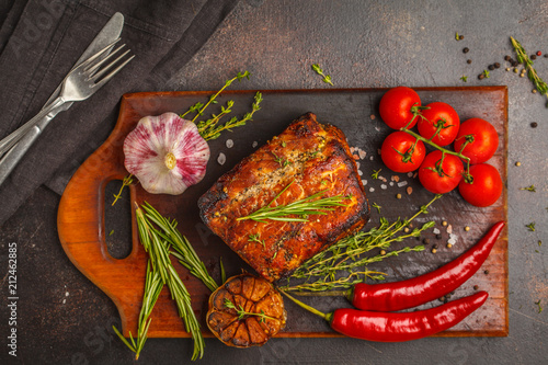 Whole piece of roast pork  with thyme  rosemary  garlic on a wooden board  dark background  top view  copy space.