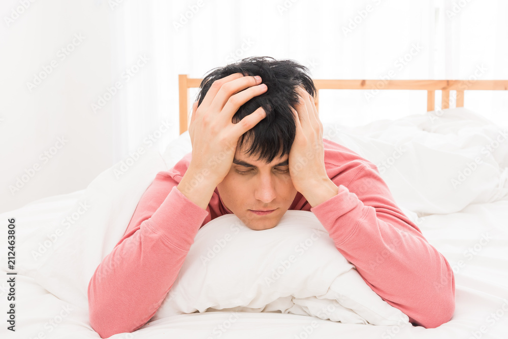 The young man was awakened by the morning alarm clock while on the bed.Shallow depth of field.unhappy from noisy sound of alarm clock and trying to turn it off. Hangover,lazy and sleepless concept.