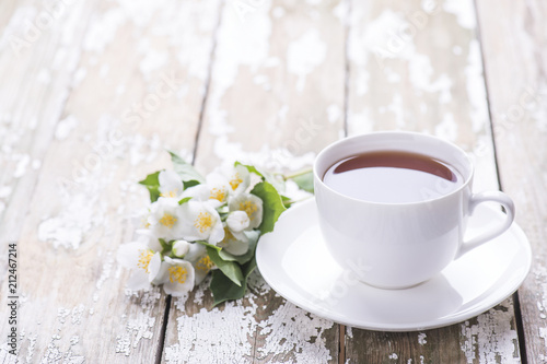 Green tea in the white cup with flowers of jasmine on a wooden old background.