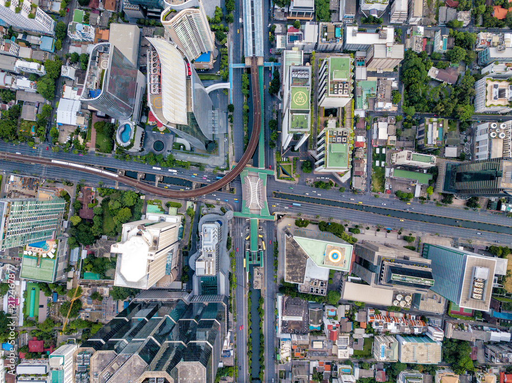 Top view of city road junctions in heart of business center on sathorn and silom district at Bangkok city Thailand. Aerial view of BTS Skytrain run into the smart city at Bangkok downtown in Thailand.