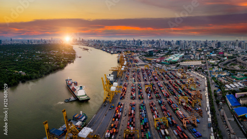 Aerial view of international port with Crane loading containers in import export business logistics with cityscape of Bangkok city Thailand at sunset