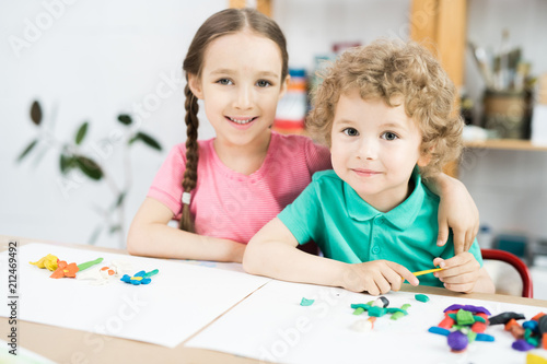 Portrait of two happy kids smiling at camera while sitting at table in art and craft lesson of development school