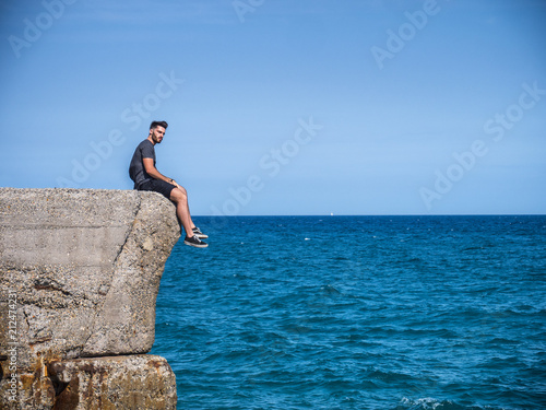Shirtless Young Handsome Man Sitting at the Beach Boulders