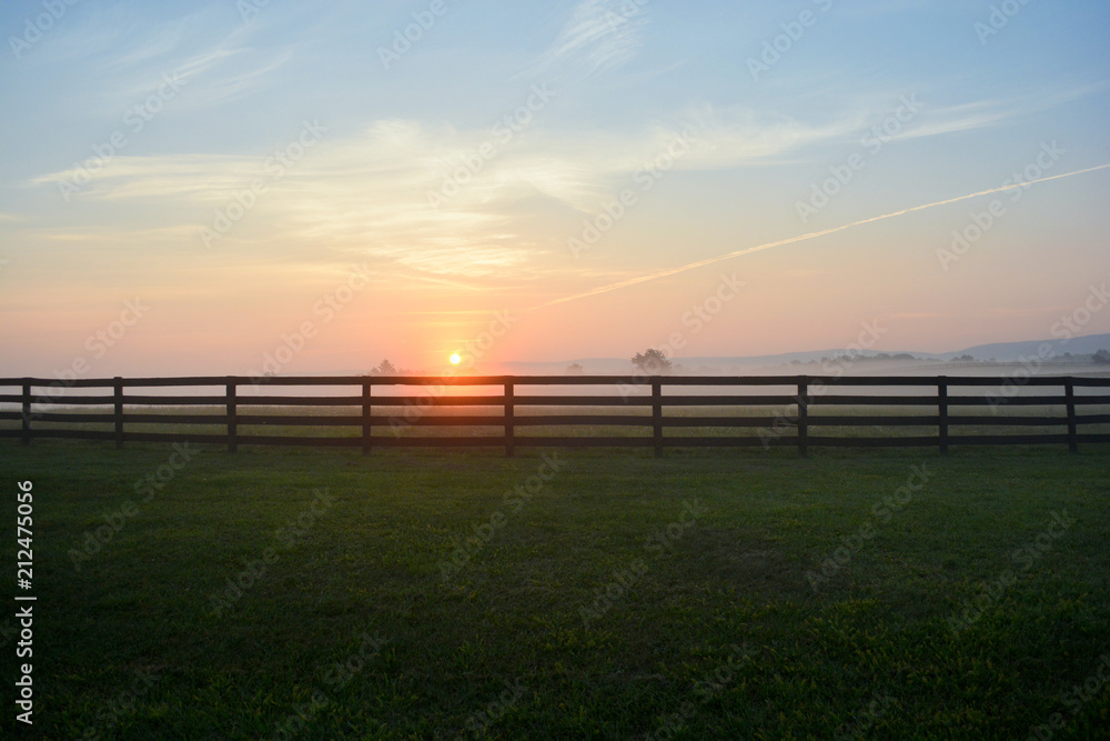 Gorgeous sunrise on a foggy morning along a black rail fence in the Virginia countryside.