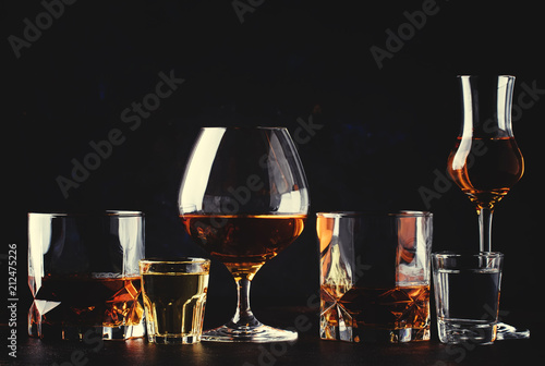 Set of strong alcoholic drinks in glasses and shot glass in assortent: vodka, rum, cognac, tequila, brandy and whiskey. Dark vintage background, selective focus