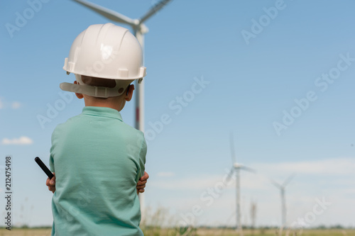 Rear view - a little boy in a blue shirt - the future engineer looks in the direction of the windmills dreaming of creating them in the future.