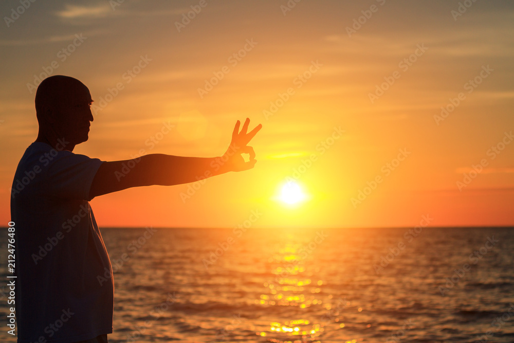 a man on the beach at sunset shows his hands how happy he is with the concept of travel and relaxation