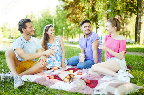 Happy and friendly teens with drinks spending leisure in park on hot summer day