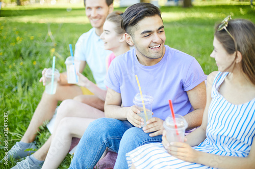 Cheerful teen couple with drinks talking at picnic on summer day with another couple on background © pressmaster