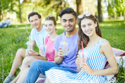 Two young couples with drinks looking at you during rest in natural environment