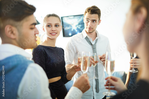 Young couple with flutes of champagne listening to one of friends toast at party