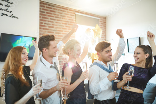 Row of cheerful dancing friends with flutes of champagne enjoying home party