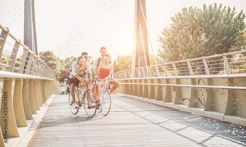 Happy friends going with bicycles on  city park - Young people having fun in sunny day after univerity - Youth, friendship and healthy lifestyle concept - Main focus on right couple photo