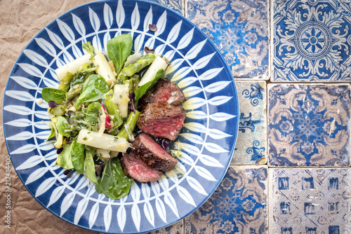 Traditional spring salad with barbecue dry aged sliced fillet steak and green and white asparagus as top view on a plate with copy space right