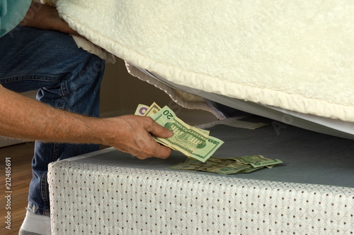 Foto Man stashing putting money under his mattress because he doesn't trust banks and is fearful of financial institutions, this is a bad way to save your money for retirement