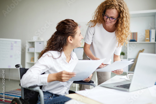 Two young businesswomen discussing papers and consulting about information
