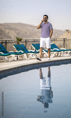 middle aged arab man by a pool, talking on a phone © katiekk2