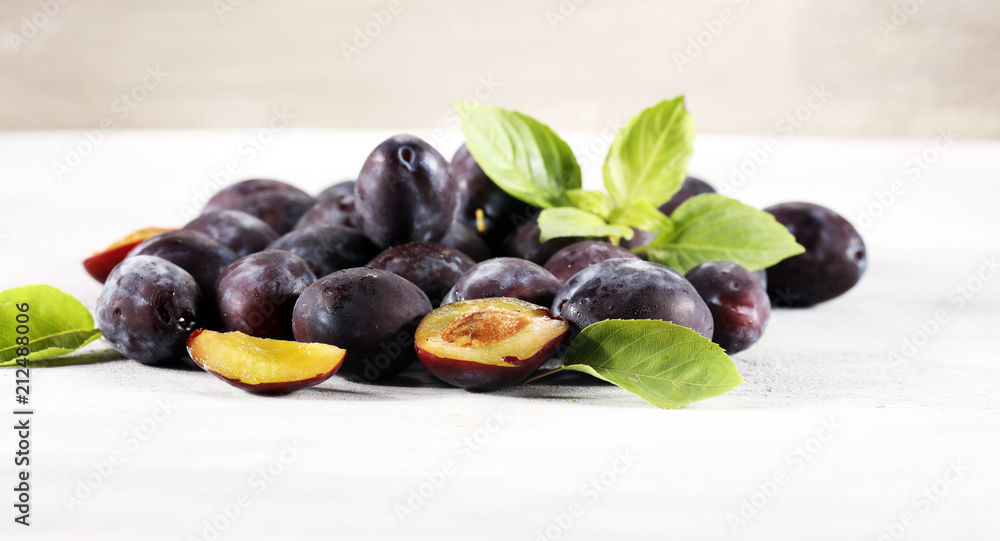 Plums on white stone background. Half of blue plum fruit. Many beautiful plums with leaves. Plums on white stone background. Half of blue plum fruit. Many beautiful plums with leaves.