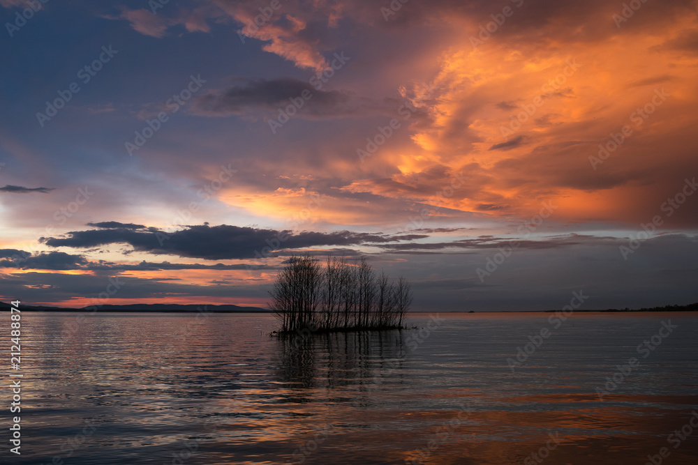 A small island with trees in the water at sunset with a red sky