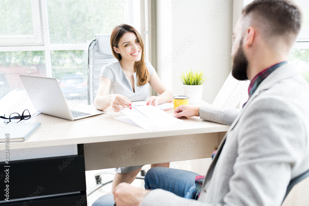 Portrait of modern female boss sitting at desk in big office smiling happily offering contract to client Portrait of modern female boss sitting at desk in big office smiling happily offering contract to client
