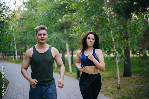 A young girl and a guy are running around the park. Doing sports outdoors. People in sportswear make a run. Leisure