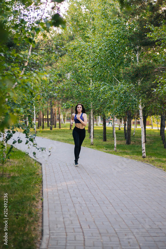 Young beautiful girl on a run. A woman is engaged in sports in the park. Healthy lifestyle. Running along the path with headphones, listening to music.