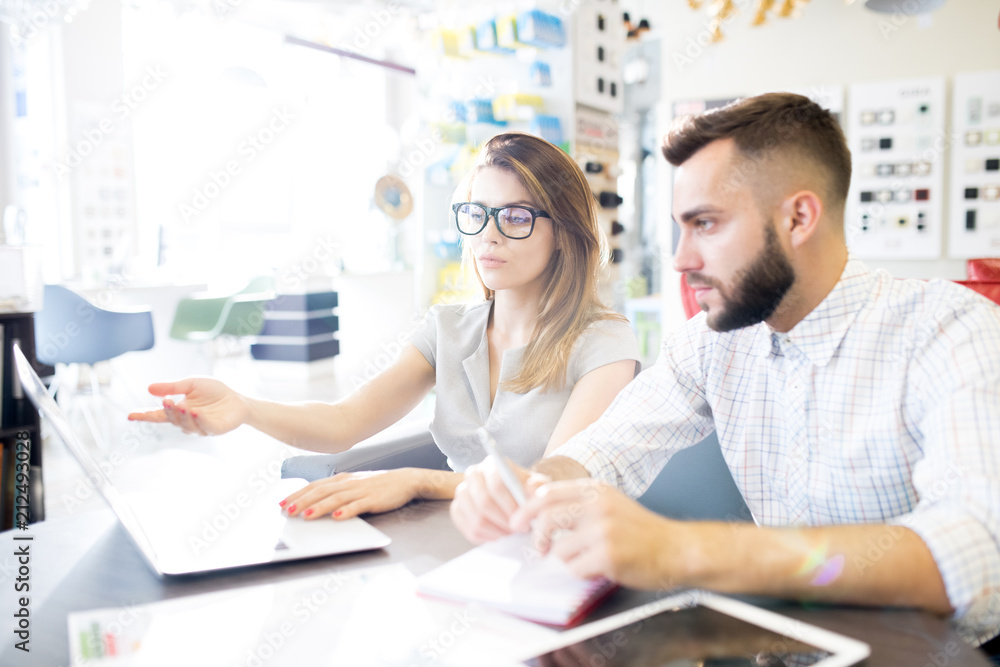Portrait of two business managers, man and woman, sitting at desk using laptop in sunlit store and planning work, copy space Portrait of two business managers, man and woman, sitting at desk using laptop in sunlit store and planning work, copy space