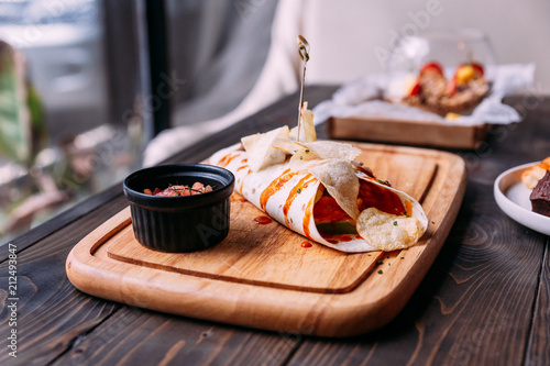 Meat kebab with chips topping with sauce and served with tomato salad on wooden plate.
