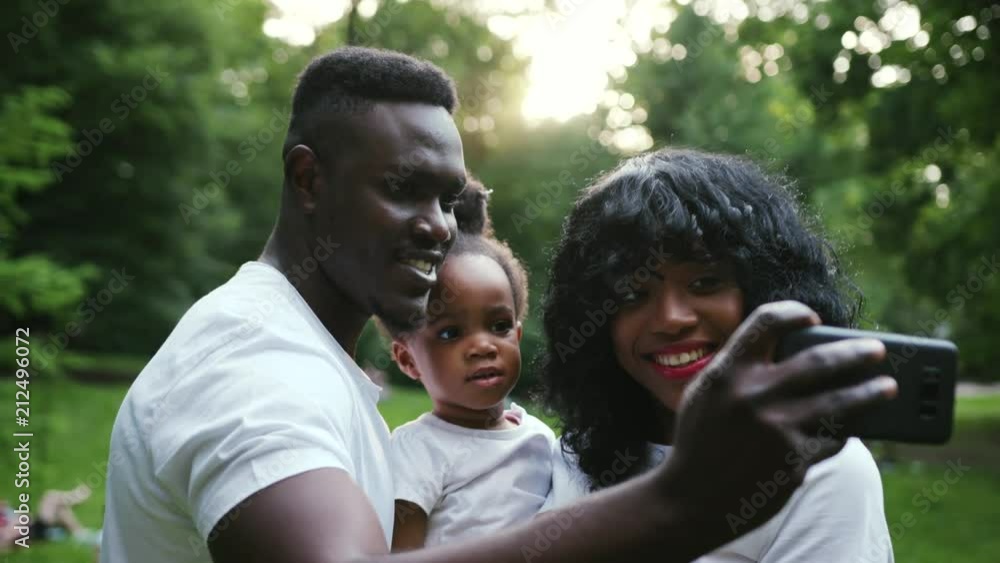 Happy african american family having fun in the park pose to take a selfie with mobile phone slow motion close up child girl daughter couple summer nature picnic mother parents portrait smartphone Happy african american family having fun in the park pose to take a selfie with mobile phone slow motion close up child girl daughter couple summer nature picnic mother parents portrait smartphone