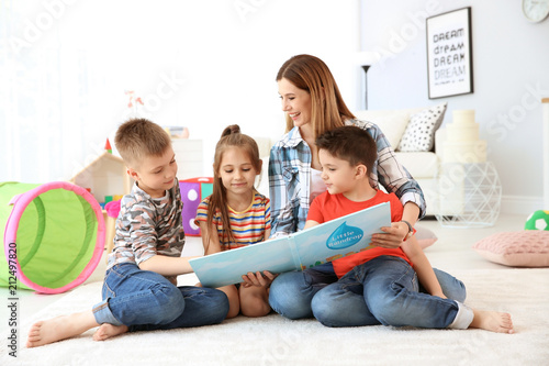 Cute little children reading book on floor with young mother in playing room
