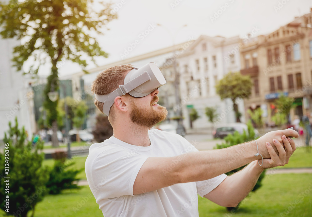 Fototapeta premium A young man plays a game wearing virtual reality glasses on the street.