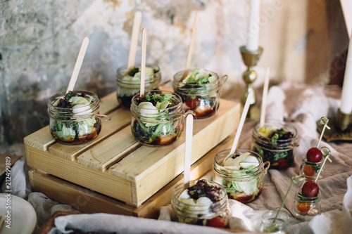 A beautiful decorated buffet table at a party with snacks in glass jars on a wooden box and canapes