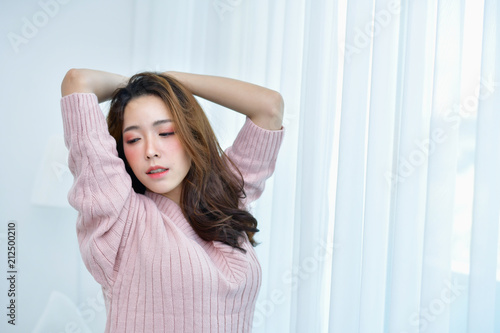 Winter Concept. Cute Asian girl in winter dress. Beautiful woman is relaxing in a bedroom. Beautiful women in winter clothes are waking up in the morning. Woman wearing a sweater in a white bedroom.