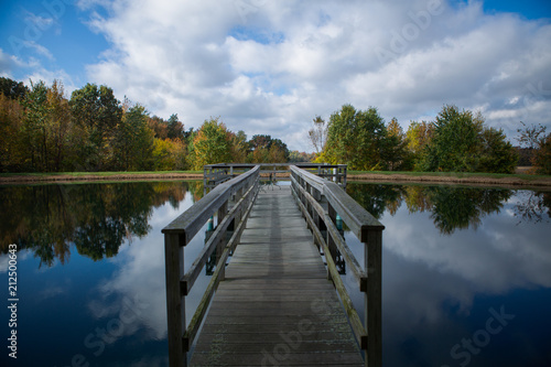 A wooden pier over a still lake in the middle of the woods in fall © Samuel