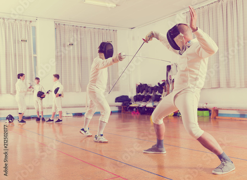 Adults and teens wearing fencing uniform practicing with foil © JackF