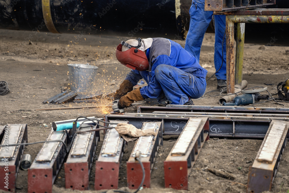 Worker grinds steel sections using angle grinder Worker grinds steel sections using angle grinder