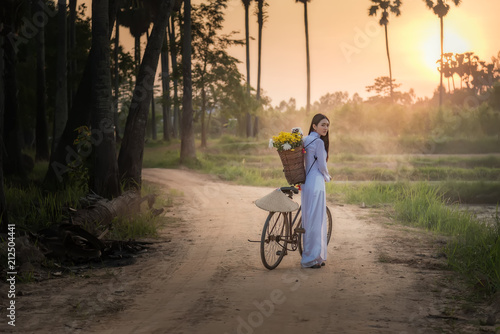 Woman wearing a Vietnamese dress Ao Dai are ride on a bicycle along the road in a village at countryside,Woman Vietnam ride on a bicycle.