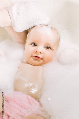 Happy laughing baby taking a bath playing with foam bubbles. Little child in a bathtub. Infant washing and bathing. Hygiene and care for young children. face of a little baby in the bathroom