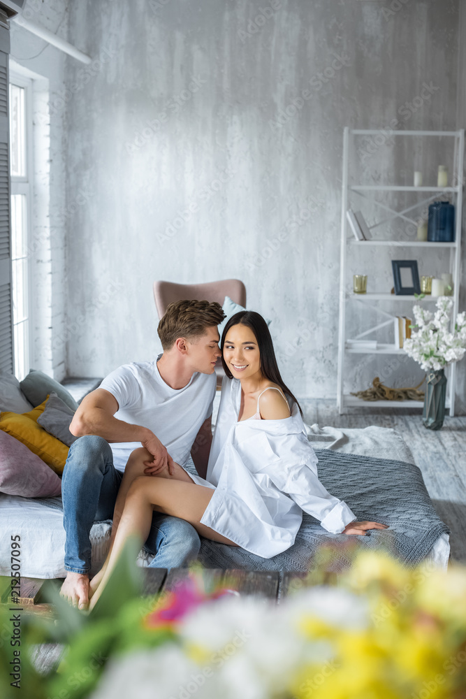 Obraz premium young multicultural couple sitting on bed in morning in bedroom