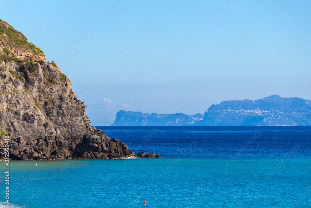Ischia Italy coastline with rocky cliffs and town in the distance. 