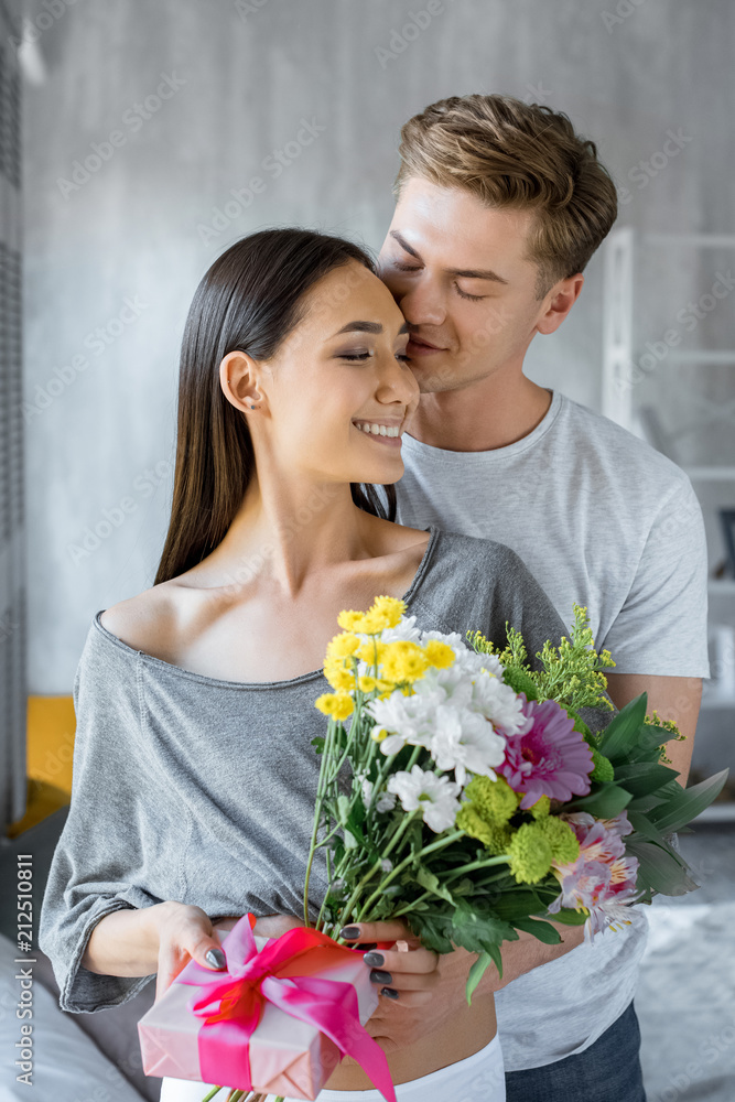 portrait of happy multiethnic couple with present and bouquet of flowers at home portrait of happy multiethnic couple with present and bouquet of flowers at home
