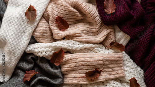 Background with warm sweaters. Pile of knitted clothes with autumn leaves, warm background, knitwear, space for text, Autumn winter concept. Copy Space.
