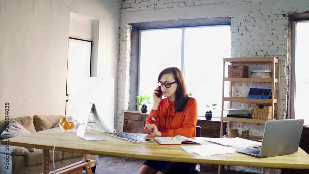 Female office assistant making phone call. Gorgeous business lady sitting at office desk working while talking over mobile phone in modern office environment. Female office assistant making phone call. Gorgeous business lady sitting at office desk working while talking over mobile phone in modern office environment.