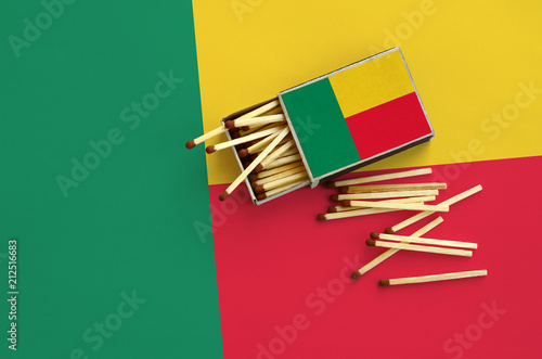 Benin flag  is shown on an open matchbox, from which several matches fall and lies on a large flag photo