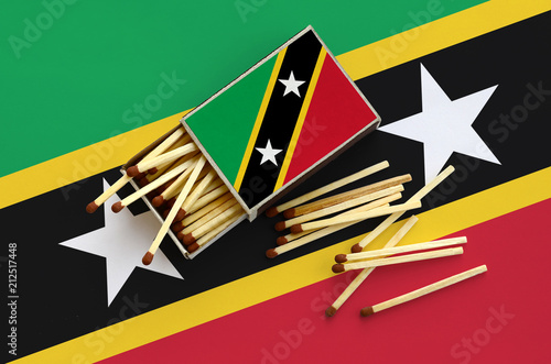 Saint Kitts and Nevis flag  is shown on an open matchbox, from which several matches fall and lies on a large flag photo